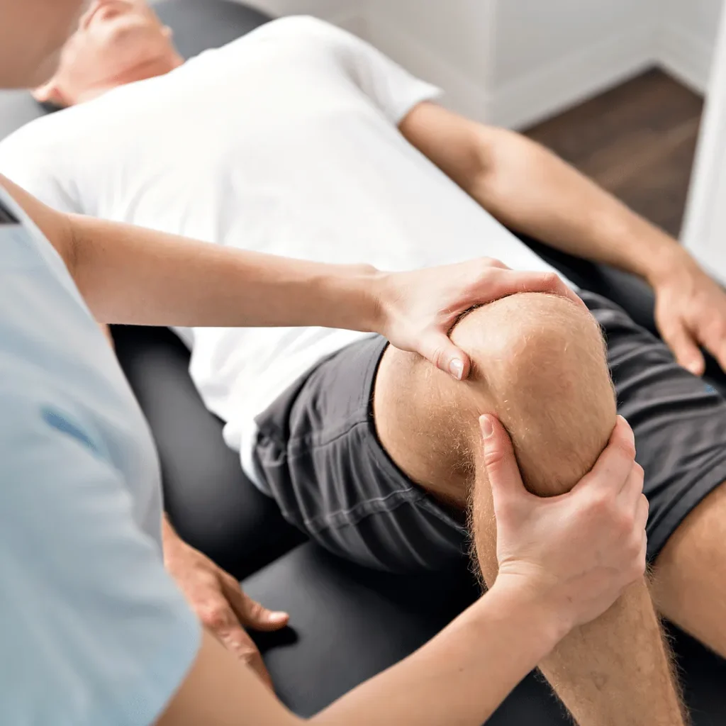 Physiotherapeut mobilisiert das Knie eines liegenden Patienten