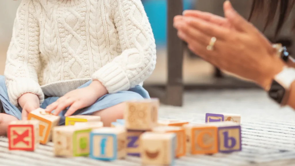 Kleinkind spielt mit Holzbauklötzen, daneben eine Erwachsene