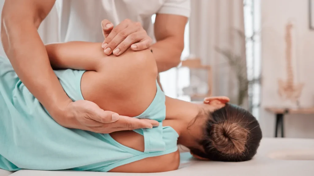 Physiotherapeut behandelt die Schulter einer liegenden Patientin in Sportkleidung